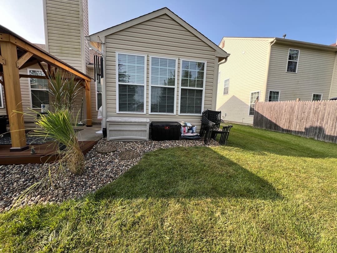 Backyard view featuring a house with large windows, patio furniture, and landscaped grass area.