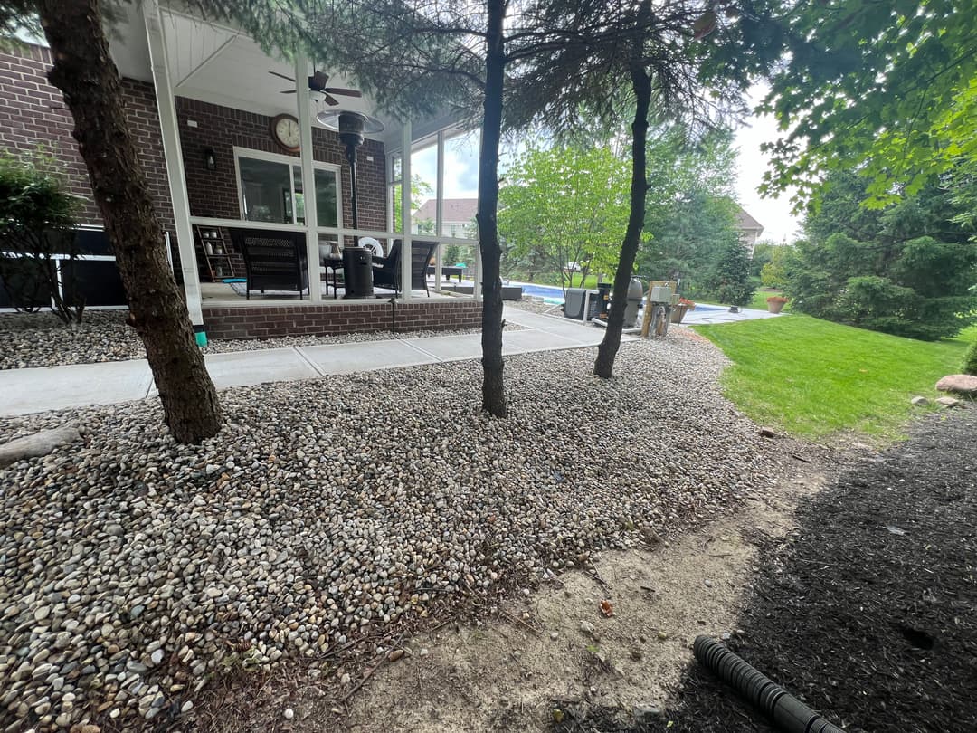 Landscape featuring pebbled area, trees, and a patio with outdoor furniture.