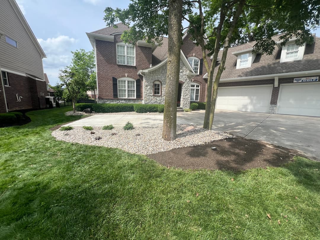 Landscaped front yard with trees, gravel beds, and a well-maintained lawn near a brick house.