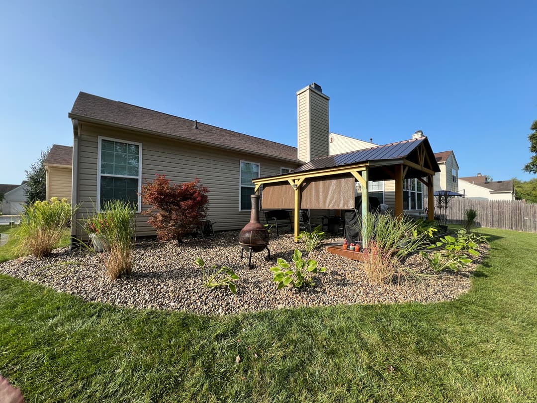 Backyard view featuring a gazebo, landscaped garden, and stone pathway under clear blue sky.