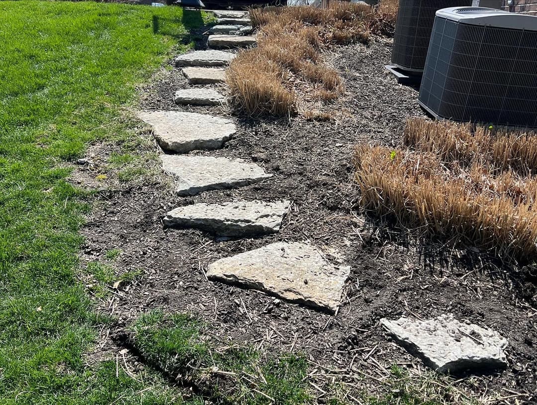 Stone walkway path through a garden with dry grass and air conditioning units.