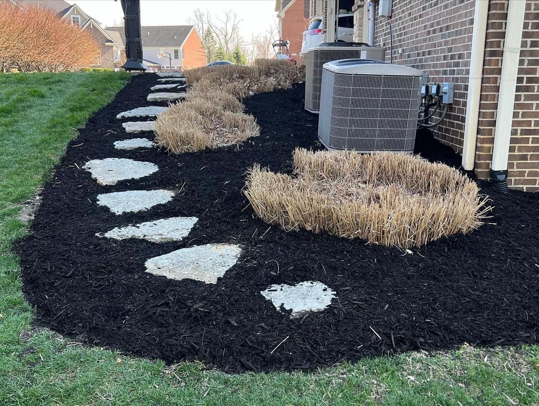 Landscaped garden featuring stone path, dried grass, and mulch near a house.