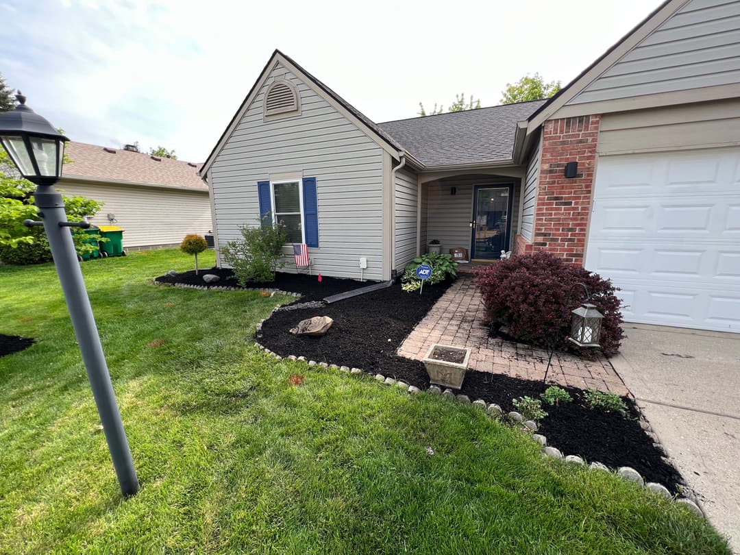 Front yard landscaping with flower beds, pathway, and decorative plants near a house.