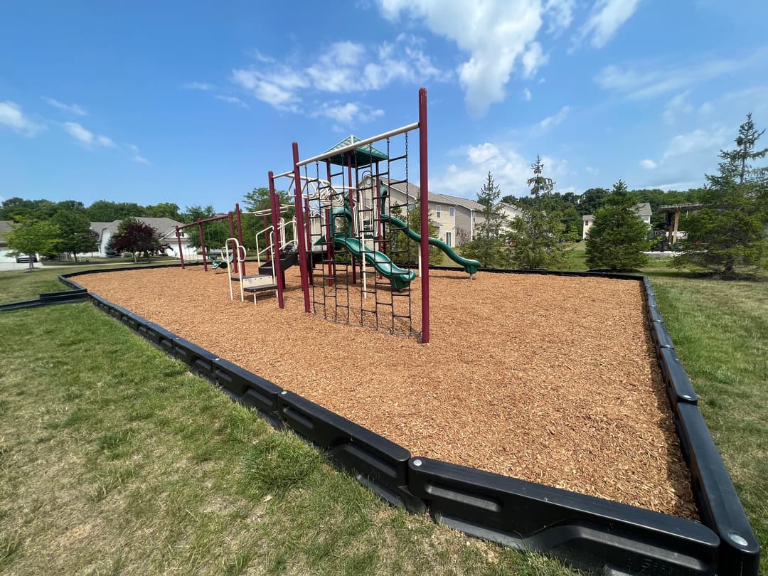 Playground with slides and climbing structures on a wood-chip surface surrounded by grass.