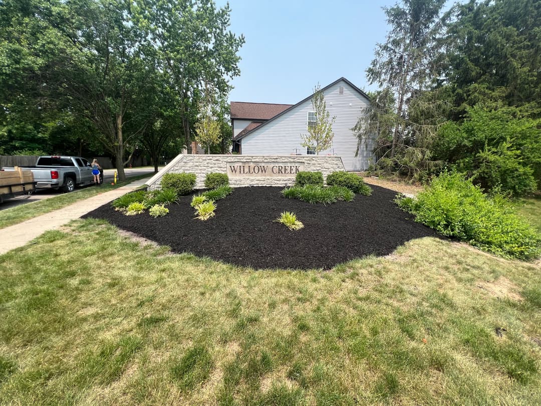 Willow Creek entrance sign with landscaped garden and trees on a sunny day.