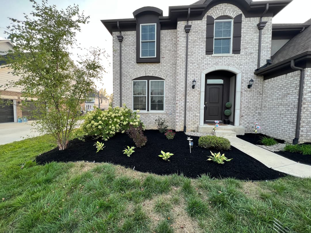 Front entrance of a home with brick façade, landscaped garden, and black mulch.