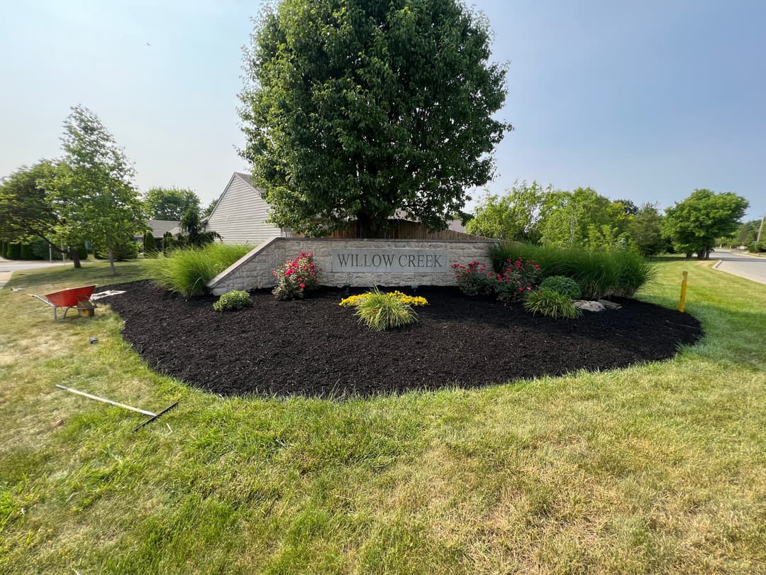 Willow Creek entrance sign surrounded by lush greenery and mulched flower beds.