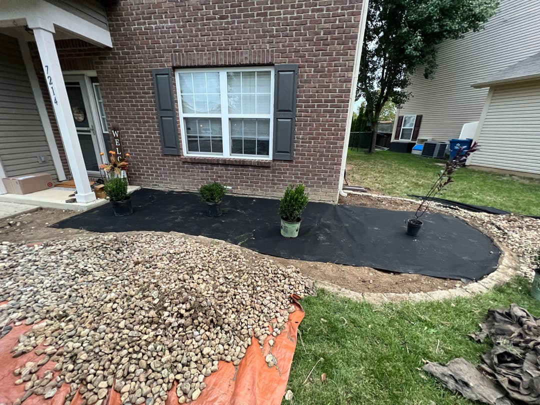 Landscape project with gravel, landscaping fabric, and potted plants near a brick house.