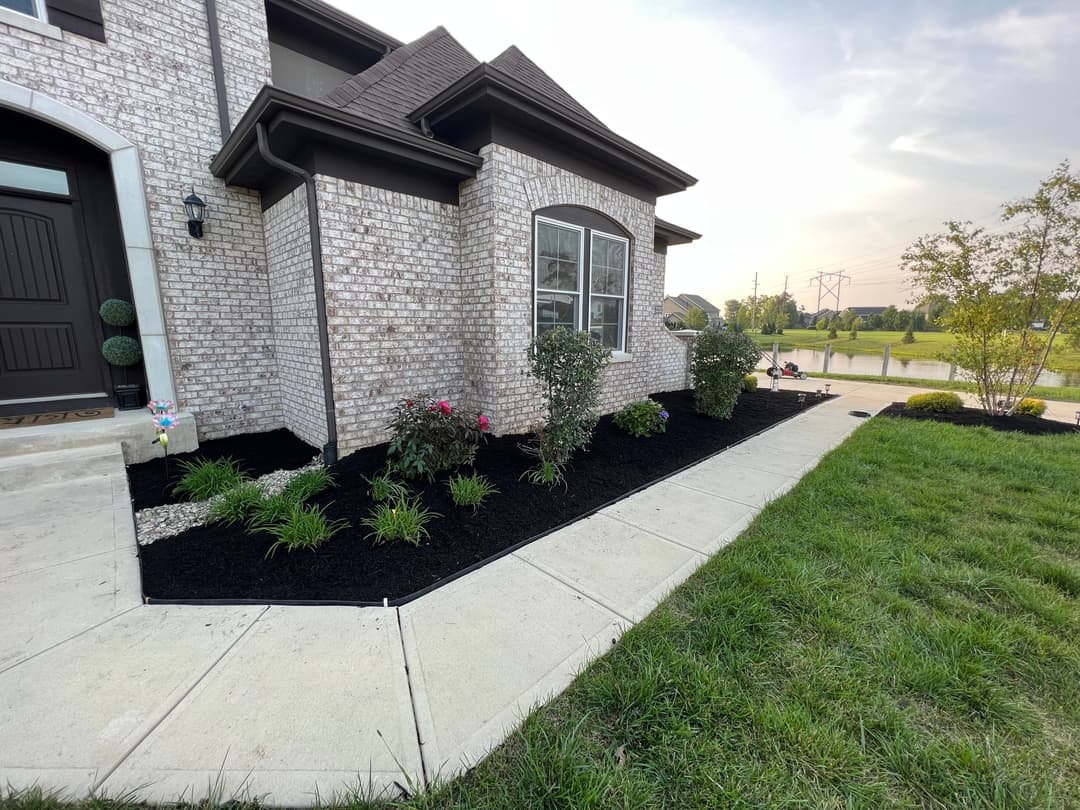 Modern home exterior with landscaped garden, black mulch, and colorful flowers.