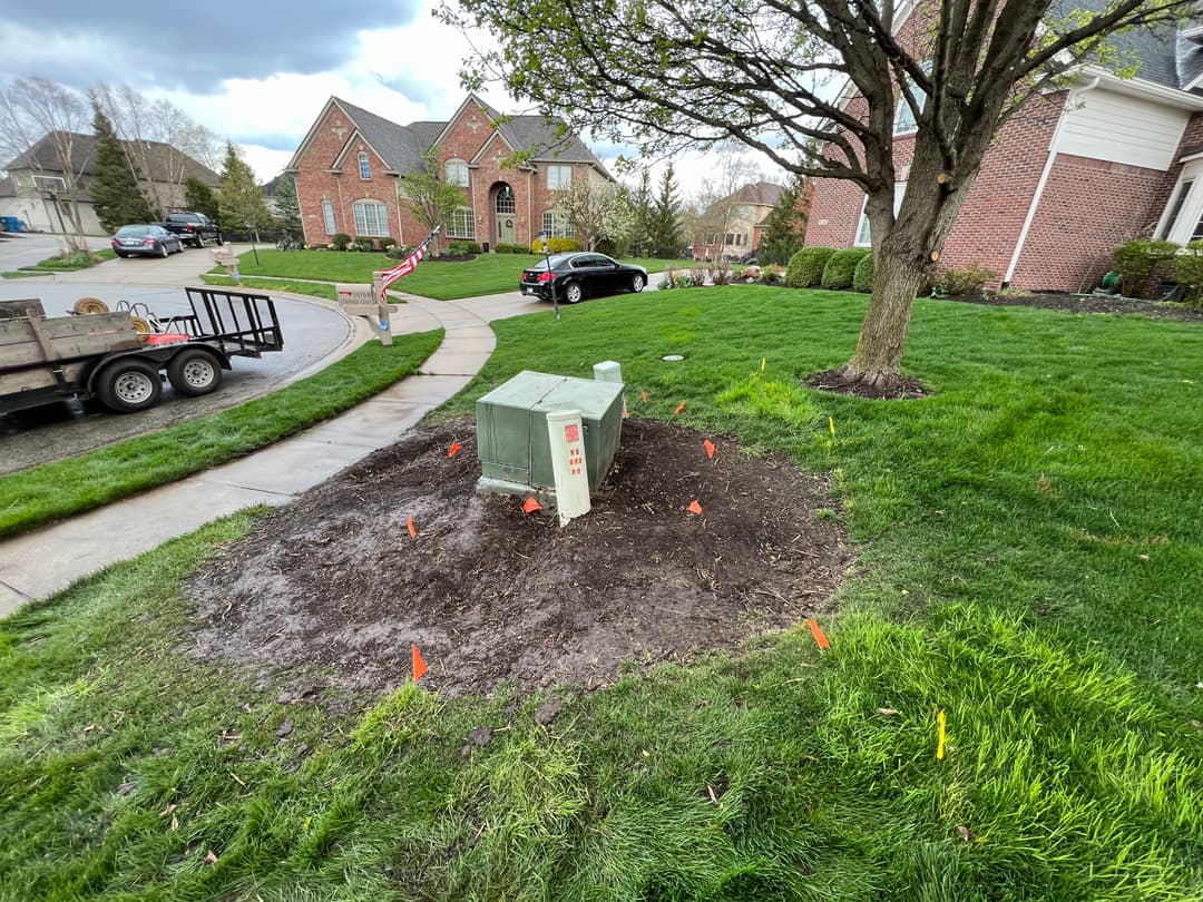 Utility box installation in a residential yard with marked stakes and freshly disturbed soil.