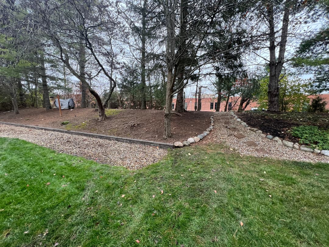 Lush backyard with gravel pathway, trees, and stone retaining wall in a residential area.