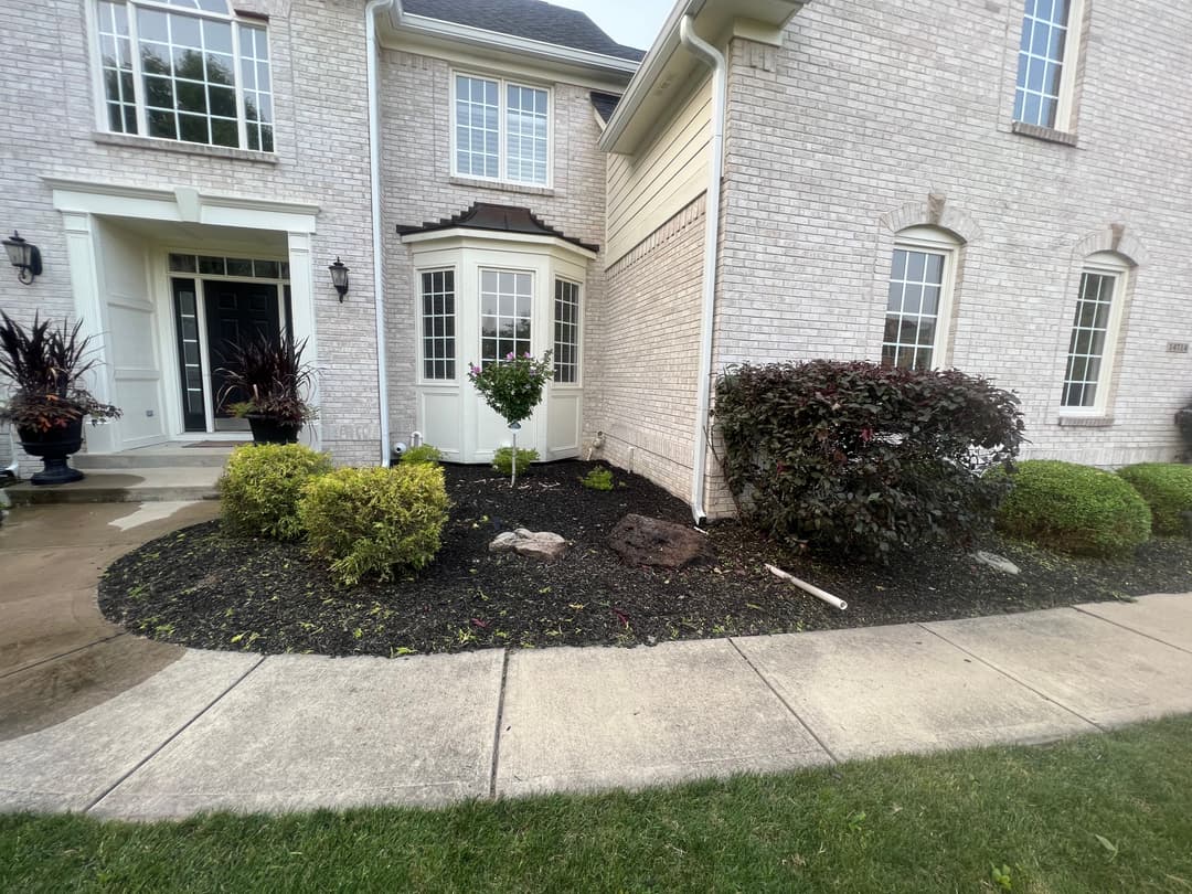 Landscape featuring a neatly maintained garden with shrubs and flowers beside a brick home.