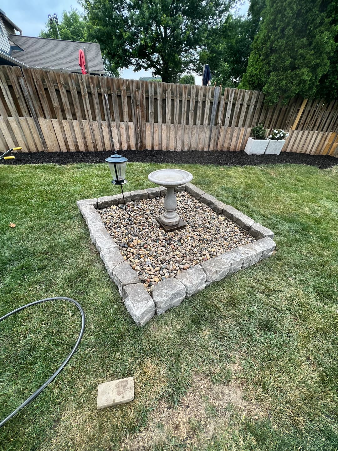 Garden birdbath surrounded by rocks, bordered by stone in a grassy backyard.