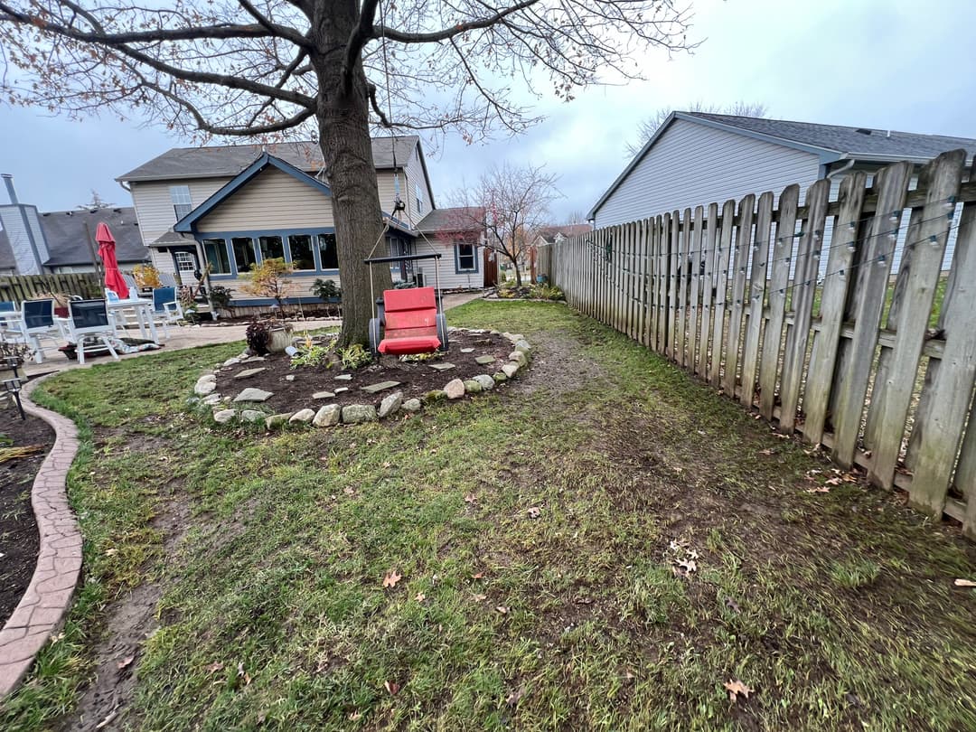 Lawn with stone circle around tree and red chair in backyard, cloudy sky in background.