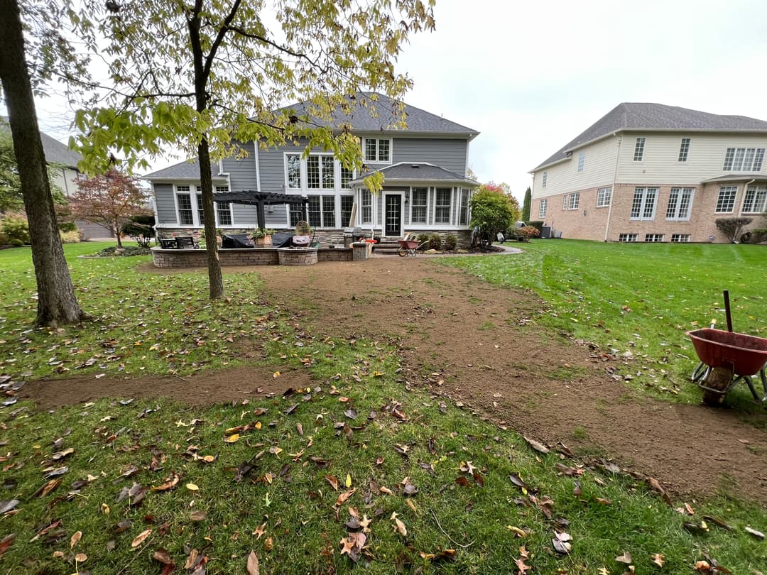 Home backyard under renovation with freshly turned soil, patio seating, and trees.