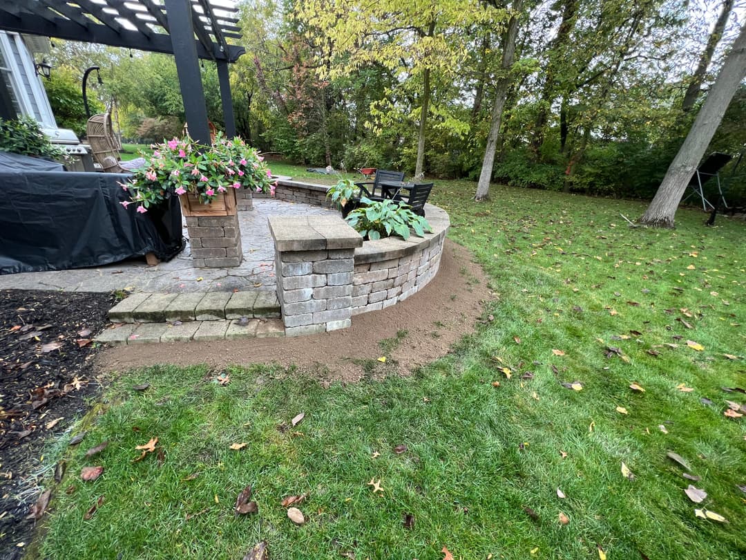 Patio area with stone wall, plants, and grass in a landscaped backyard setting.