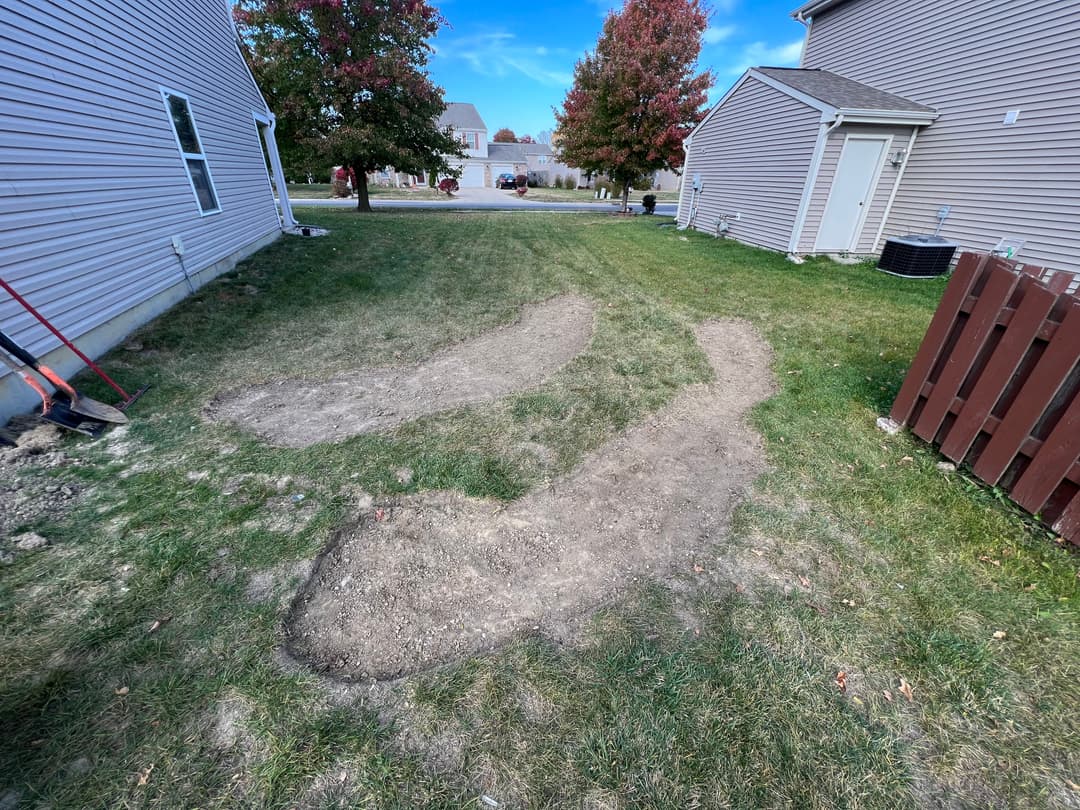 Excavated backyard area with bare soil and grass patches, illustrating landscaping work in progress.