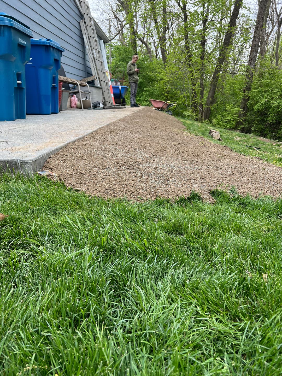 Gravel pathway beside a house, with a person working and green grass in the foreground.