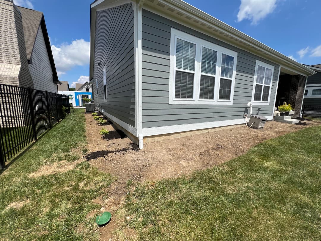 Gray house exterior with landscaped yard and clear blue sky. Side view showing gutter and fence.