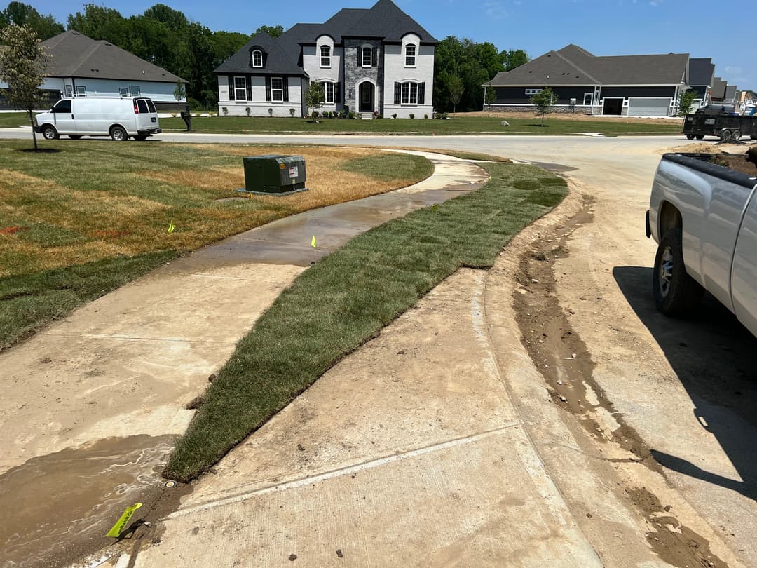 Newly installed sod curves alongside a driveway in a residential construction area.