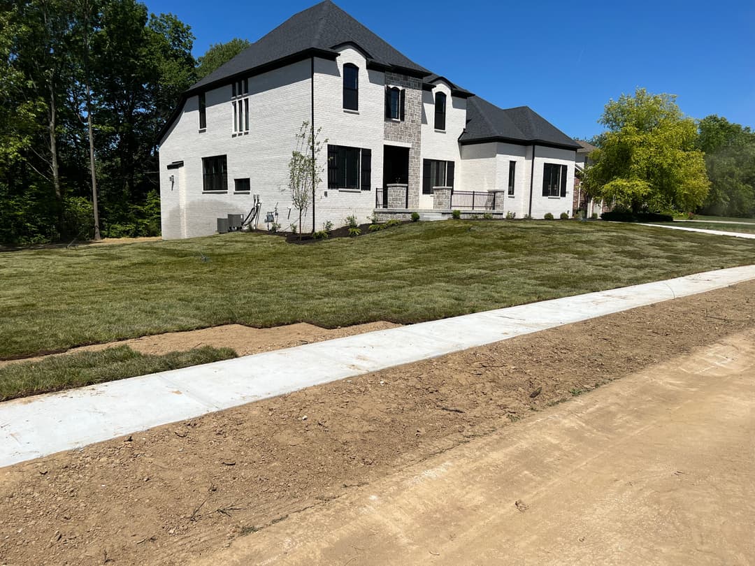 Modern two-story white brick house with manicured lawn and clear blue sky.