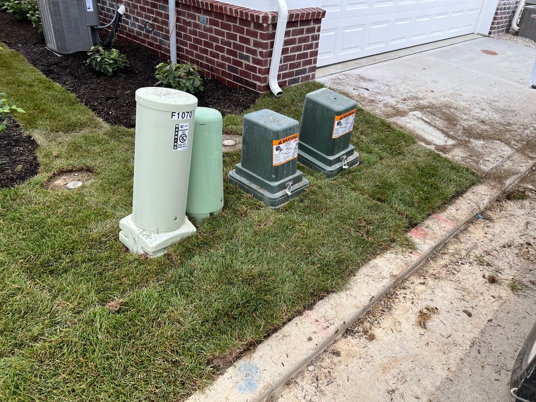 Green and white utility boxes on a lawn beside a driveway and garage.