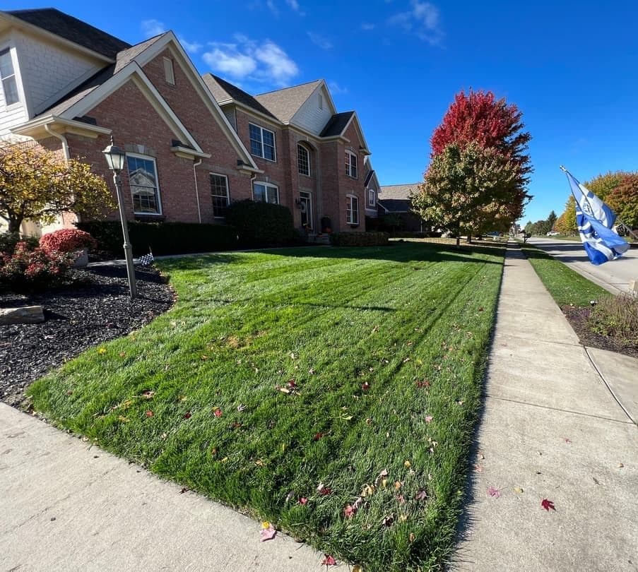 Well-maintained lawn in front of a stylish brick house with colorful autumn trees.